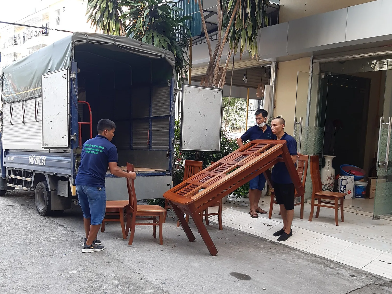 Chuyển nhà phố: bốc bàn ghế gỗ, tủ kính, giá inox, xếp kín xe tải; bên trong thùng xe xếp gọn đệm, ván, thùng 