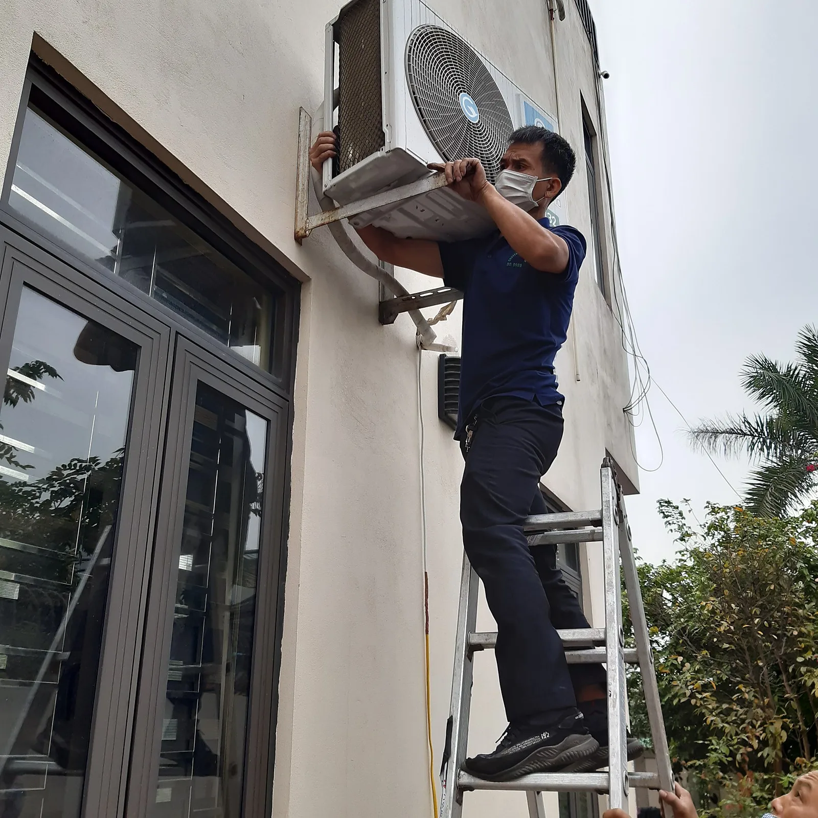 Thợ đứng thang tháo dàn nóng điều hòa trên tường ngoài nhà